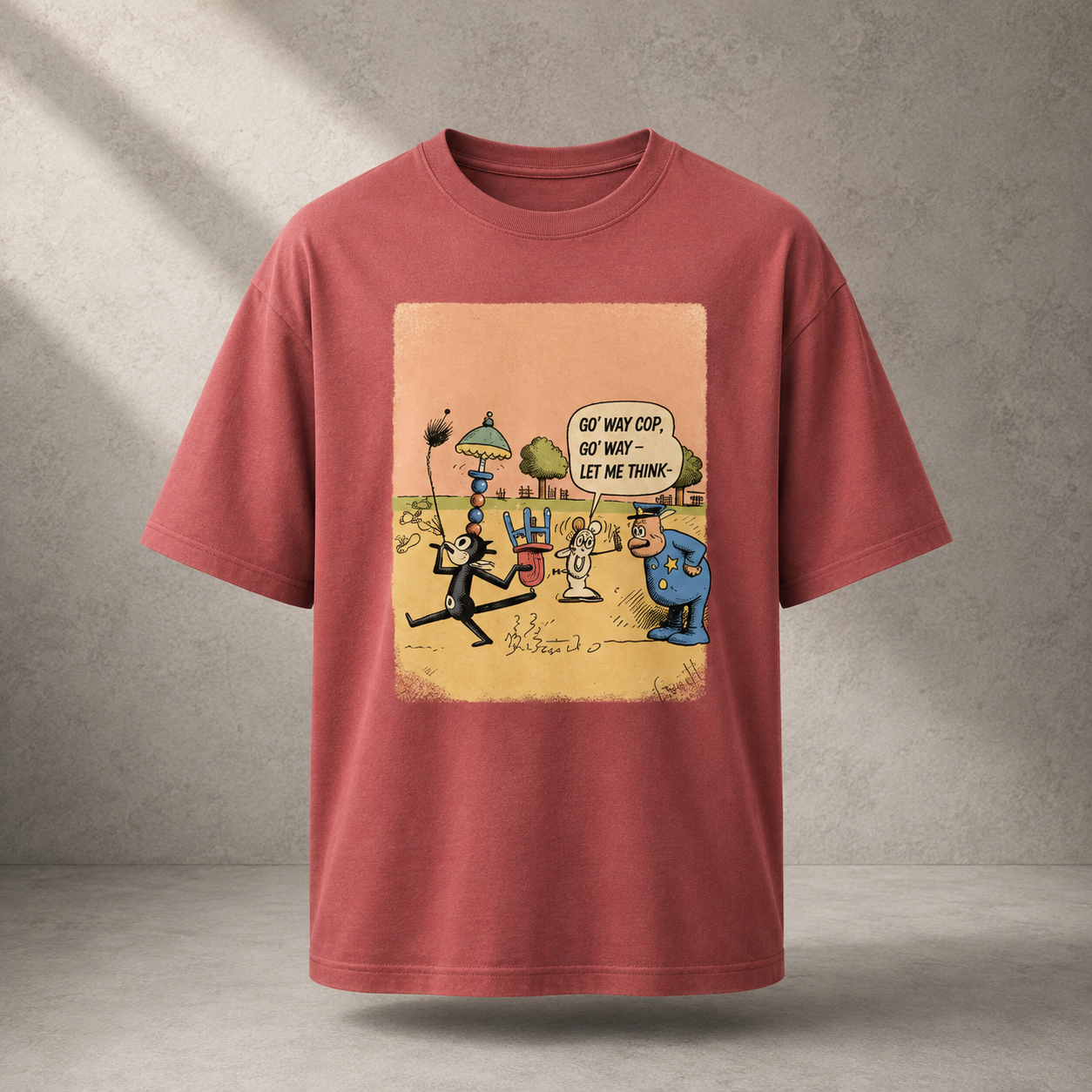 A coral colored short-sleeve t-shirt with a large cartoon graphic print on the front, displayed against a textured gray concrete wall background.