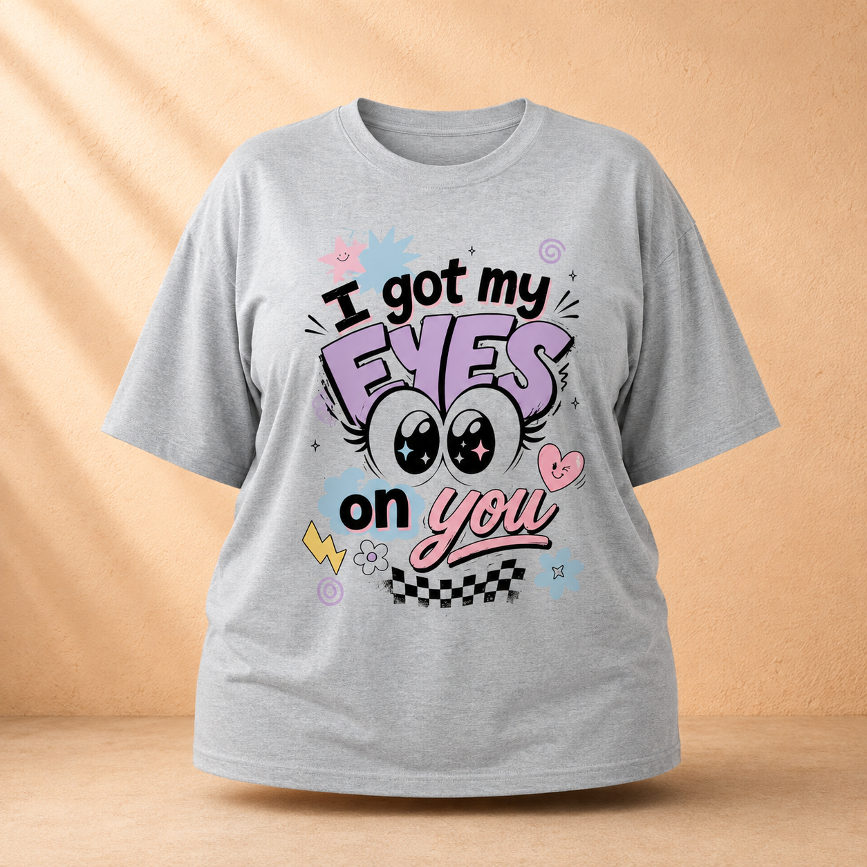 A light gray short-sleeve Oversized Classic T-Shirt with a colorful graphic print that reads 'I got my EYES on you' in stylized lettering, displayed against a warm beige background with soft shadow overlays.