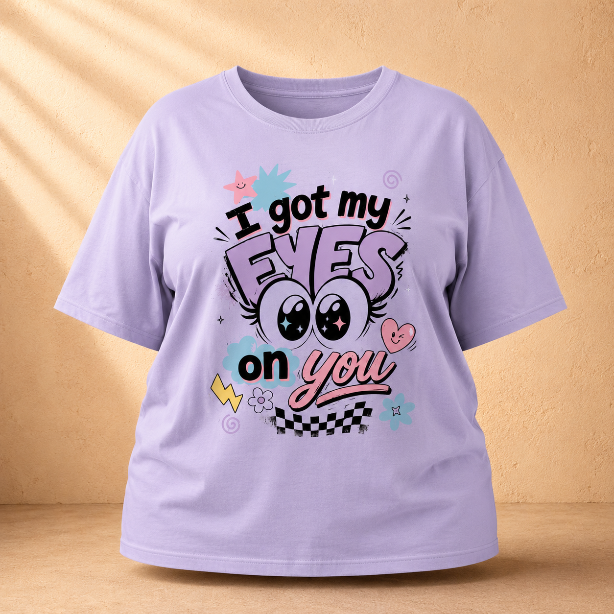 A light purple short-sleeve Oversized Classic T-Shirt with a colorful graphic print that reads 'I got my EYES on you' in stylized lettering, displayed against a textured beige background with soft shadow overlays.