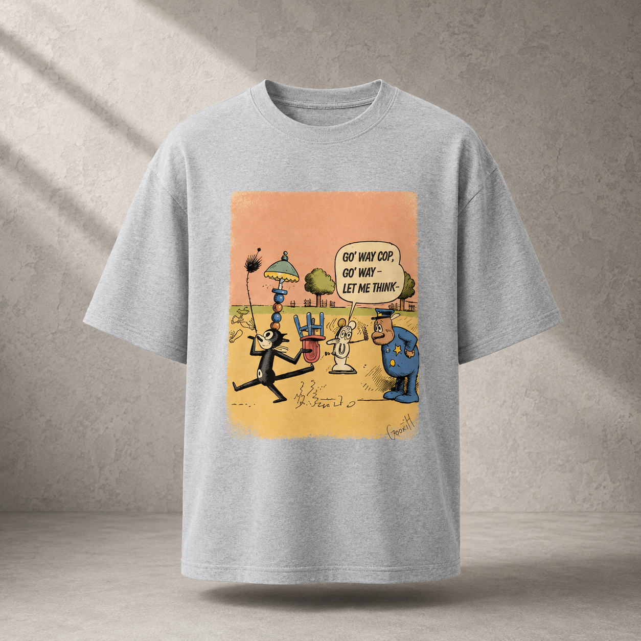 A light gray oversized short-sleeve t-shirt with a colorful cartoon graphic on the front, displayed against a textured gray concrete wall with soft diagonal shadows.