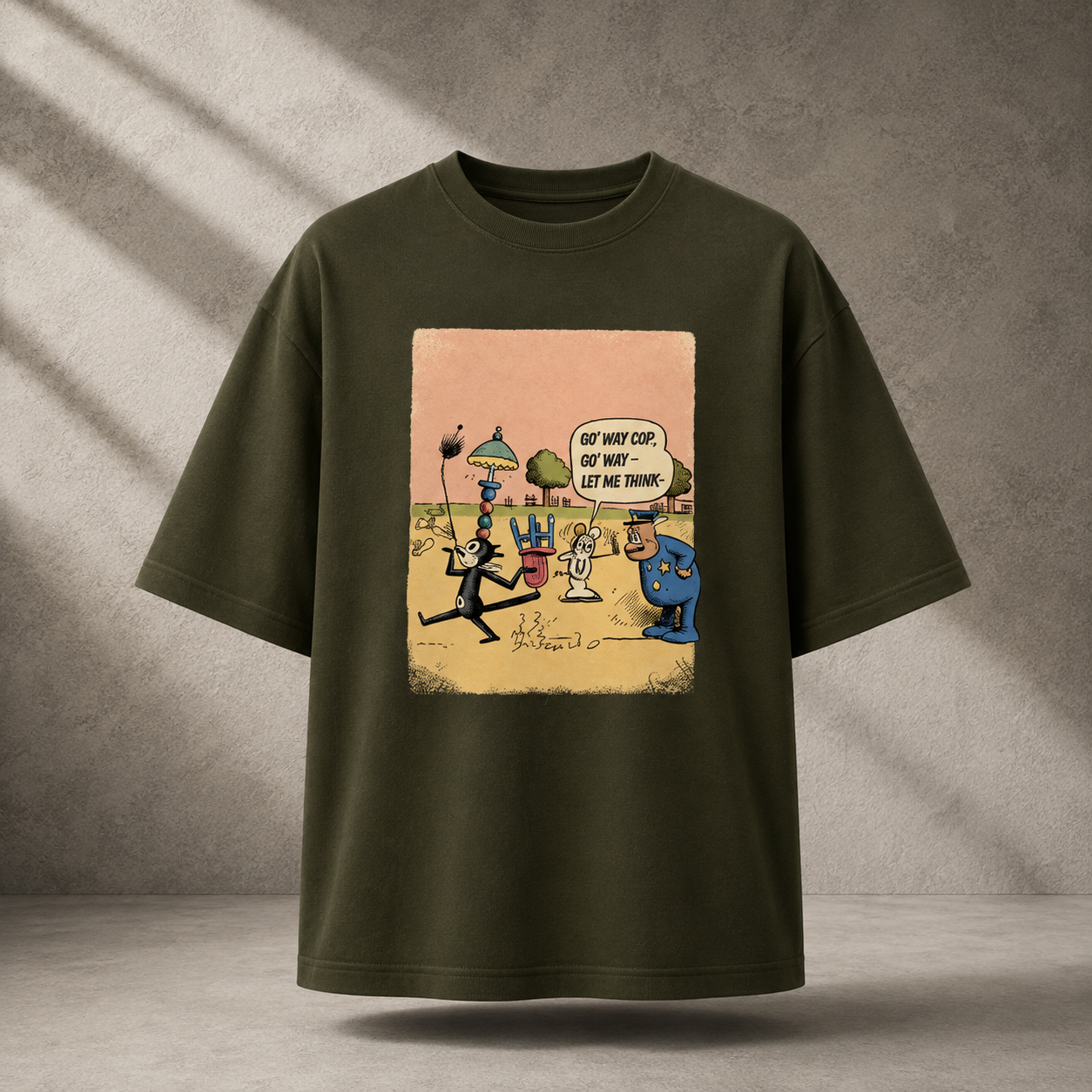 An oversized olive green t-shirt with a colorful cartoon graphic print on the front, displayed against a textured gray concrete wall with diagonal shadows.